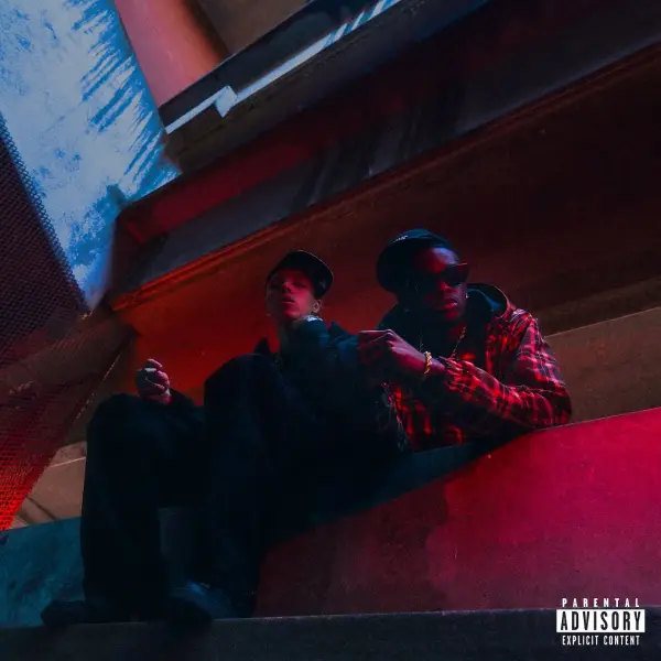 Two men in streetwear sit on a red ledge under dramatic urban lighting.