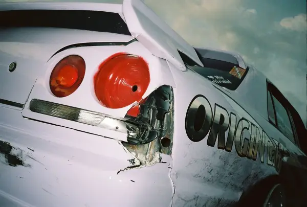 A close-up shot of a white sports car with significant body damage and red taillights.