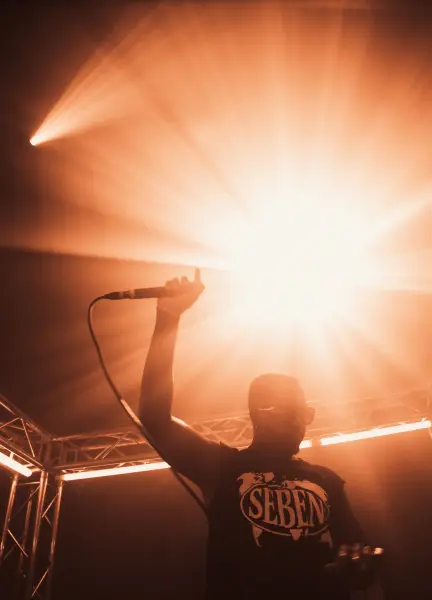 A silhouette of a performer holding a microphone against a bright orange stage light.