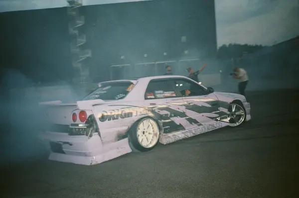 A modified white sports car drifting through a cloud of tire smoke.