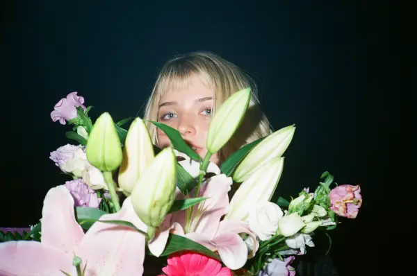 A young woman with blonde hair peeking through a large bouquet of pink and white lilies.