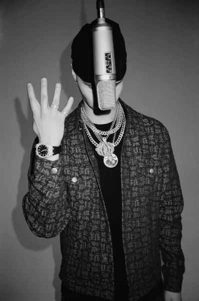 A person in a beanie and textured jacket holds up their hand near a studio microphone.