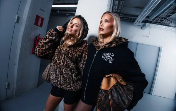 Two women posing in a hallway wearing leopard print and oversized streetwear.