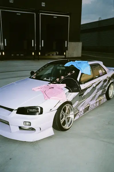 A modified white hatchback with custom decals parked in front of a modern industrial building.