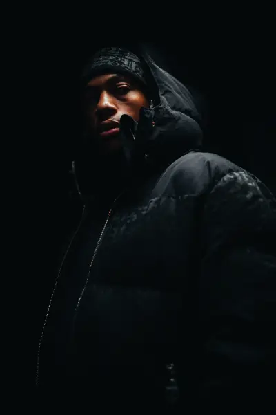 A portrait of a man wearing a black puffer jacket and beanie in low-key lighting.
