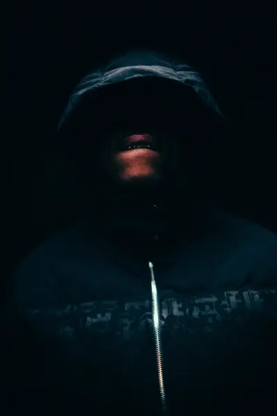 A person wearing a hoodie and a face mask obscured by deep shadows.