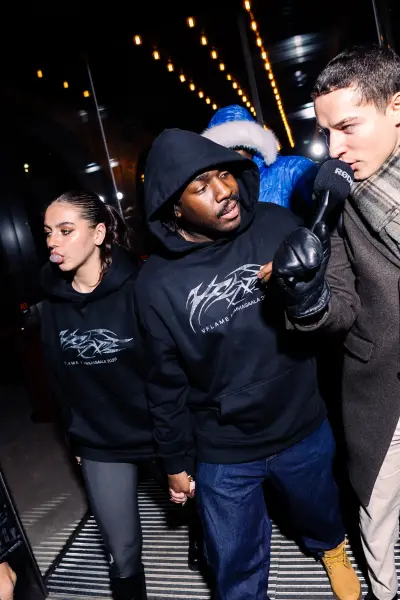 A man in a black hoodie is interviewed by a reporter on a city street at night.